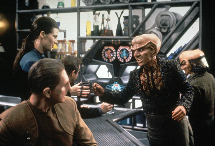 Quark hands a drink to Dax across the bar while Odo looks on